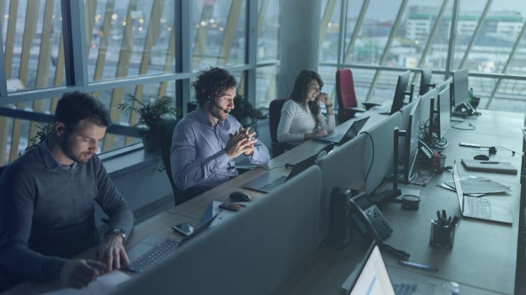 A woman points at data charts on a large digital screen while colleagues look on.