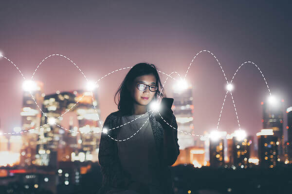 A woman using a smartphone with graphical light connections overlayed against a cityscape at night
