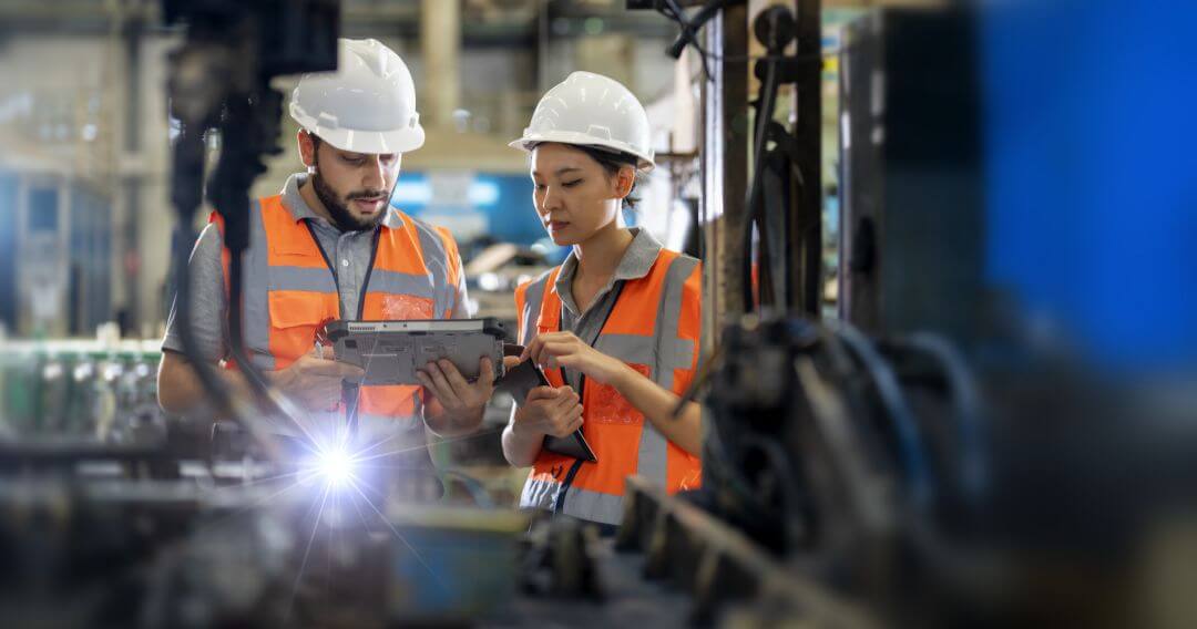 2 people wearing orange vest and helmet looking at tablet